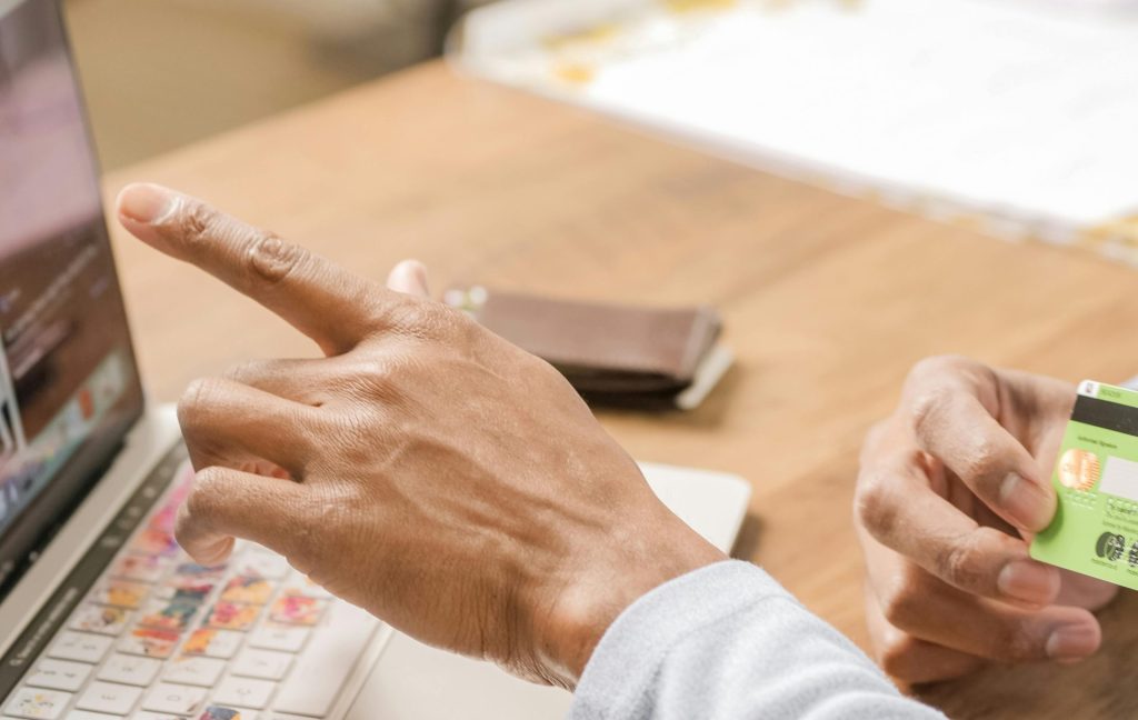 Person using a credit card and pointing at laptop for online shopping activity.